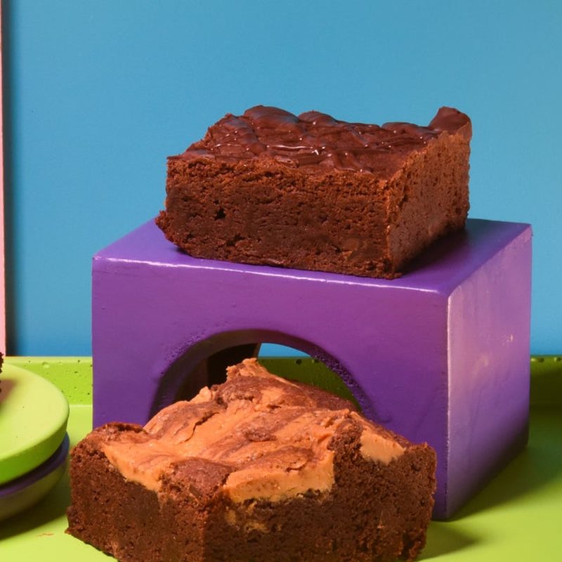 Brownies on a purple block and a green plate against a blue panel.