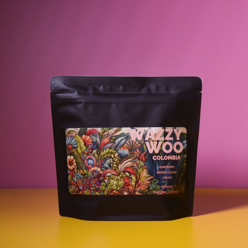 A black bag of Wazzy Woo Colombia coffee on a yellow shelf against a pink wall.