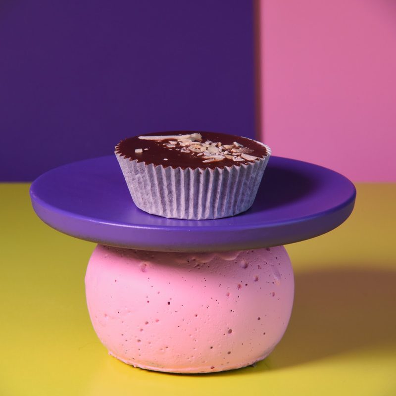 A chocolate peanut cup on a purple plate and a pink stand, against purple and pink panels.
